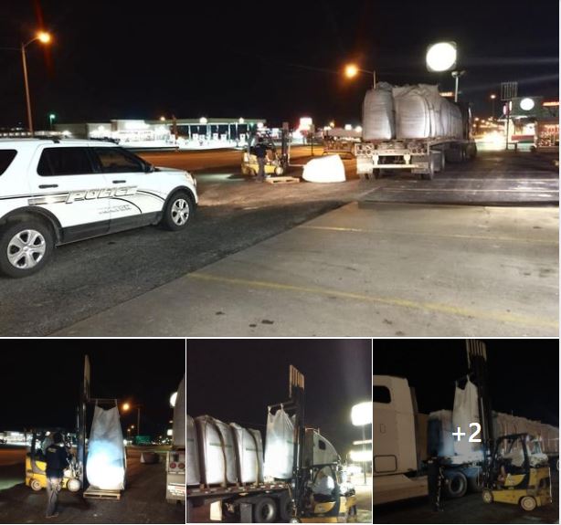 Image of a police car behind a semi truck that had dropped a bag of peat moss. A forklift can be seen getting ready to move the bag of peat moss.